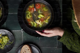 a person holding a bowl of soup on top of a table