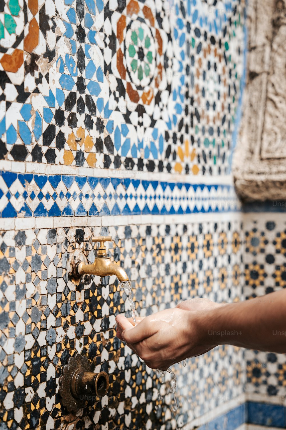 a person's hand reaching for a faucet in a tiled wall