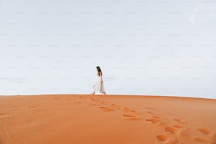 a woman in a white dress walking across a desert