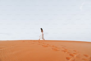 une femme en robe blanche marchant à travers un désert