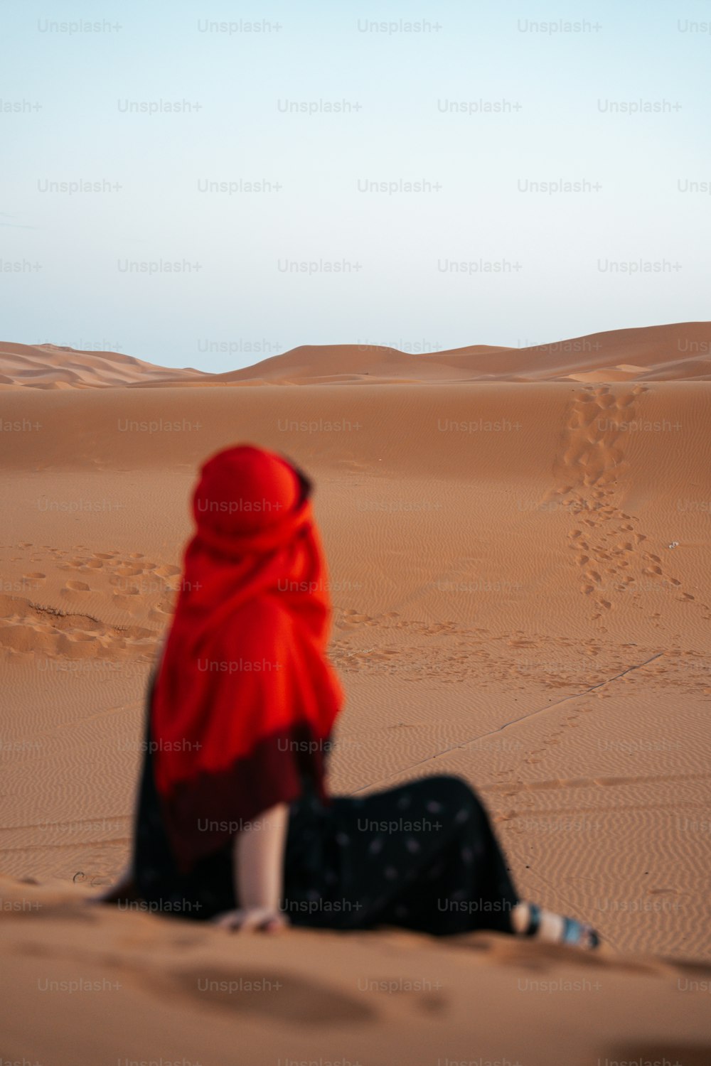 Eine Frau in einem roten Schal sitzt in der Wüste