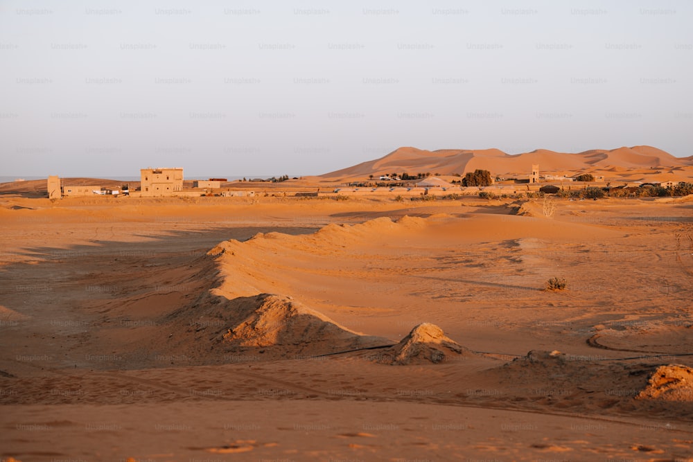 a desert landscape with sand dunes and houses in the distance