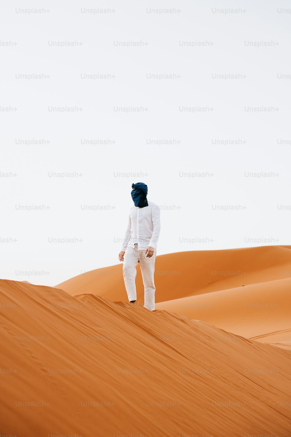 a person in a white suit standing on top of a sand dune