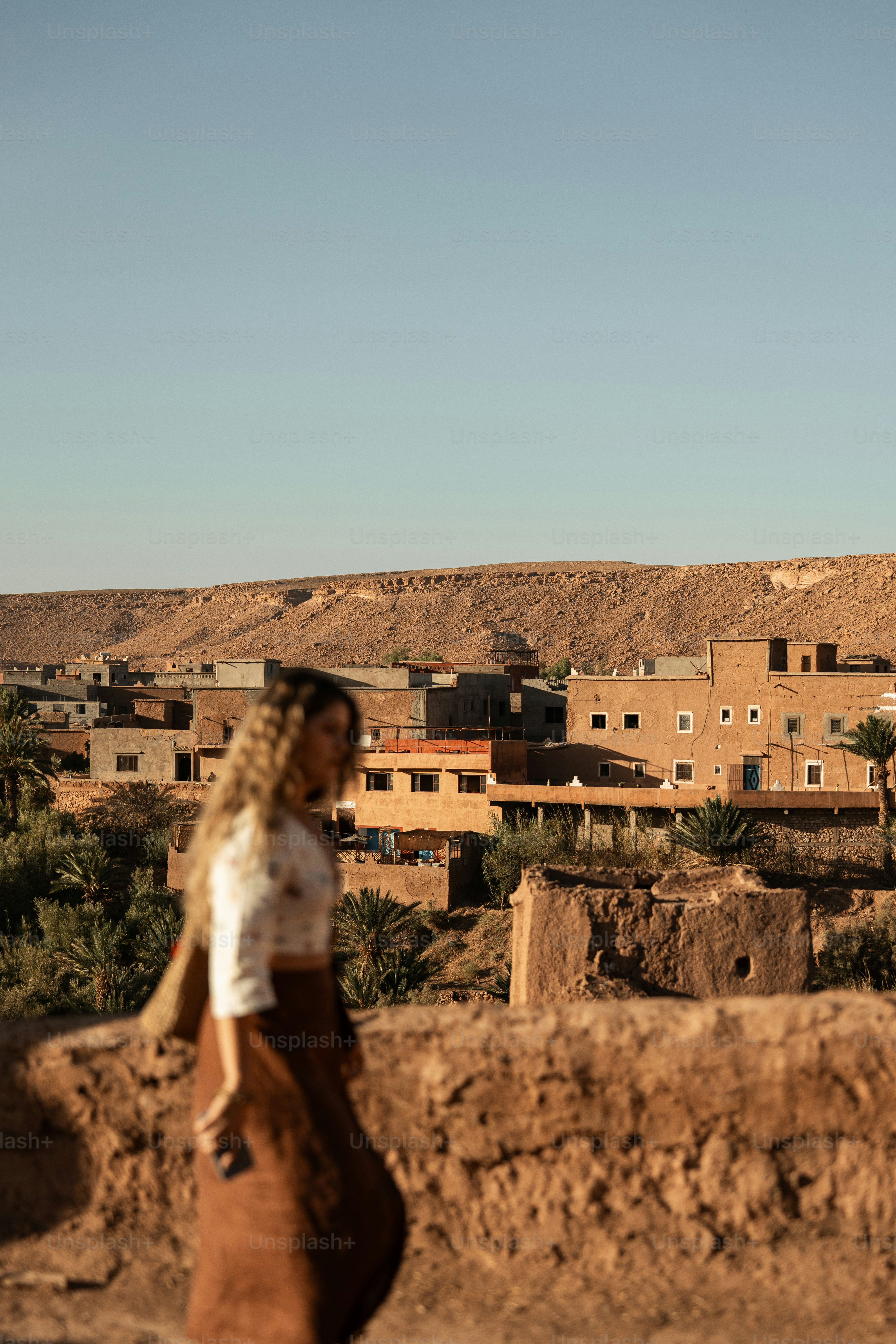 a woman walking down a dirt road next to a desert town