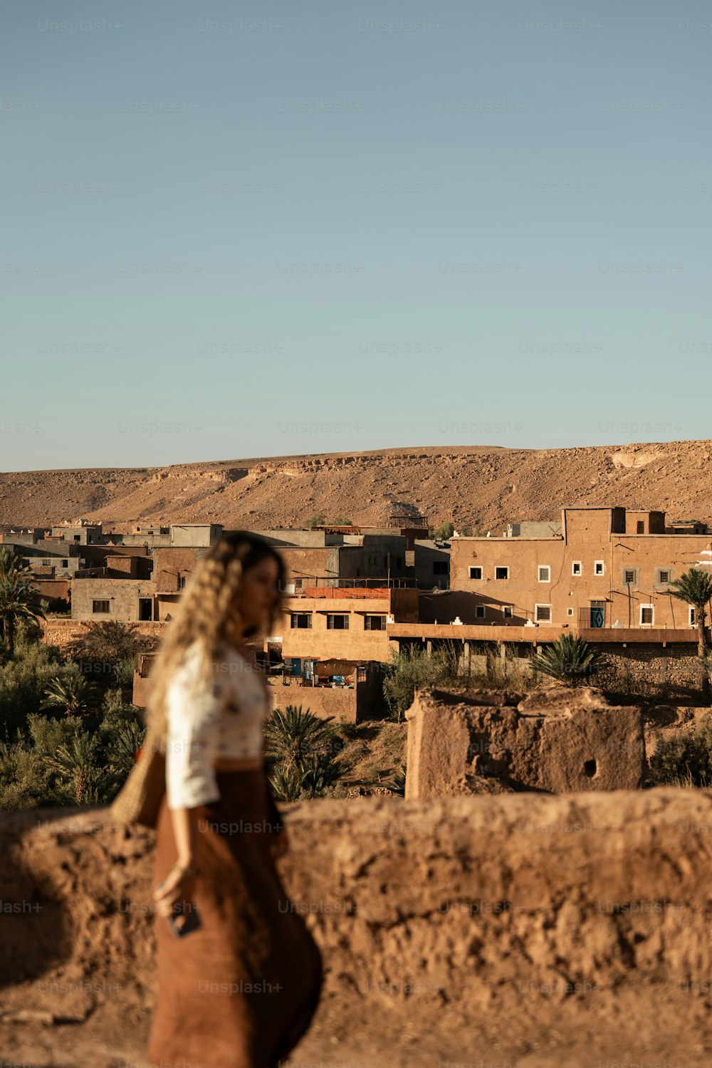 Eine Frau, die einen Feldweg neben einer Wüstenstadt entlanggeht