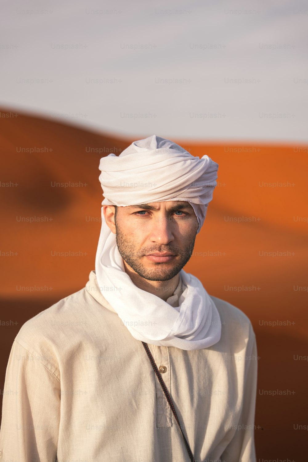um homem com um turbante branco em pé no deserto