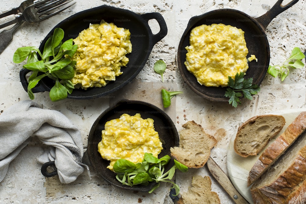 three skillets filled with scrambled eggs and bread