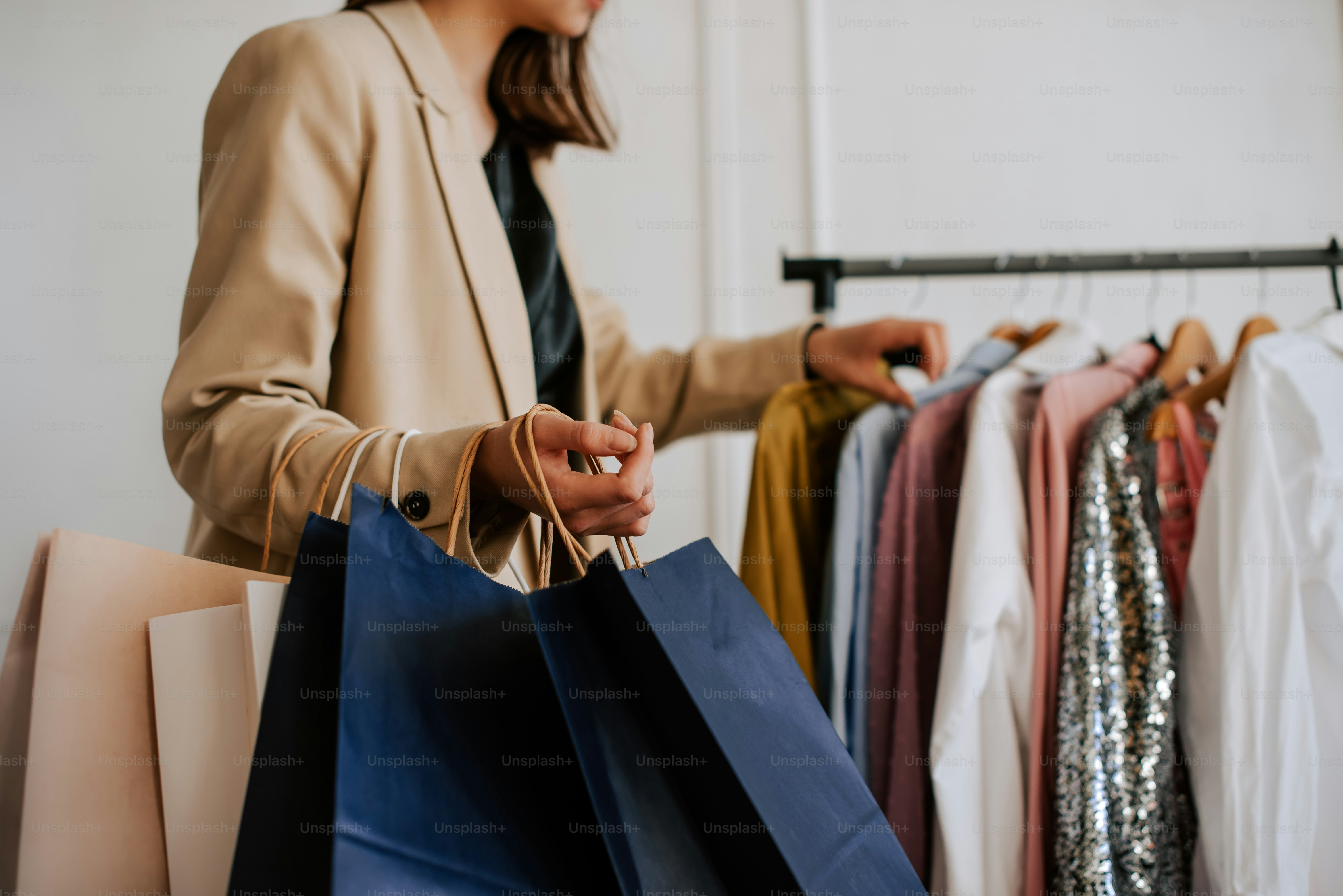 une femme tenant des sacs de courses devant un portant de vêtements