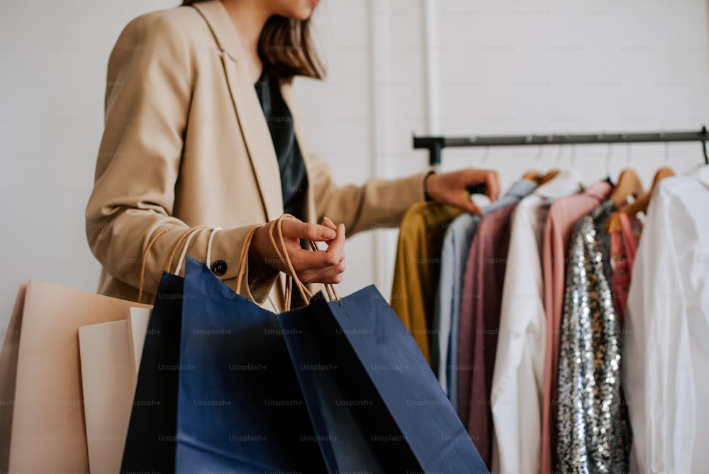 una mujer sosteniendo bolsas de compras frente a un perchero de ropa
