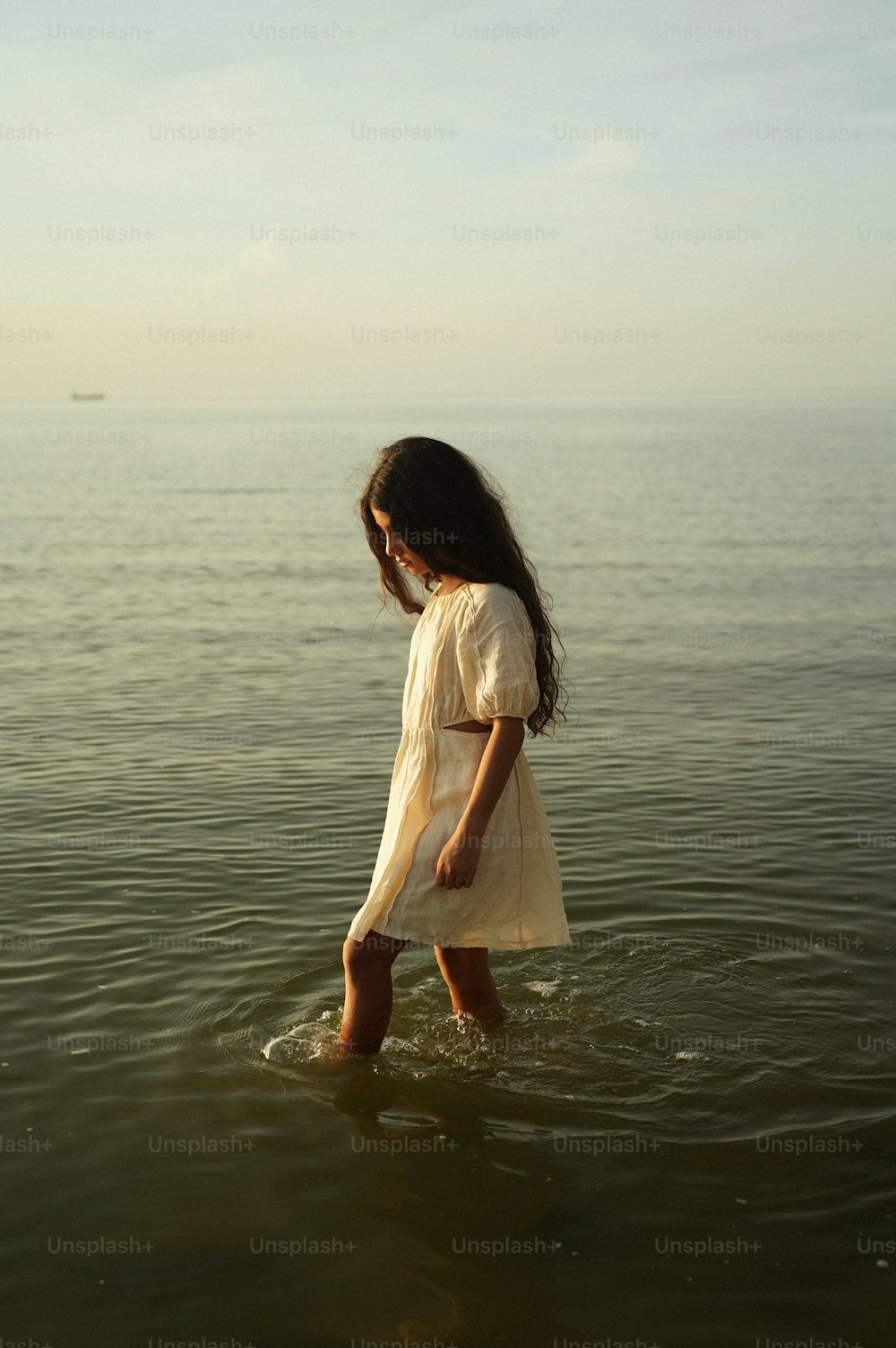 a little girl standing in the water looking at the ocean