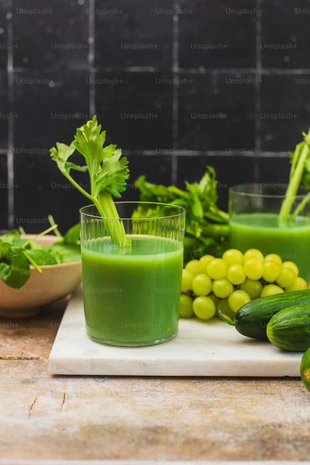 a glass of green juice next to a bowl of grapes and cucumbers