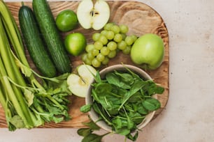 a wooden cutting board topped with green vegetables and fruit