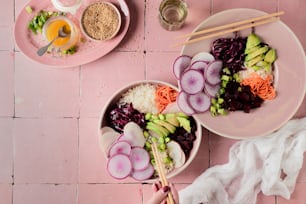 ein rosafarbener Tisch mit Tellern mit Essen und Essstäbchen