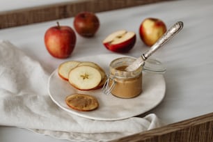 a white plate topped with apples next to a jar of peanut butter