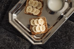 deux morceaux de pain grillé avec des tranches de banane et un verre de lait