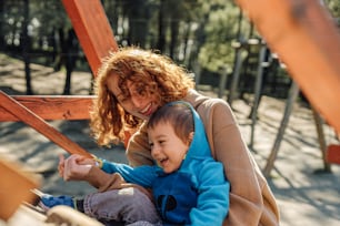 a woman holding a child on top of a wooden swing