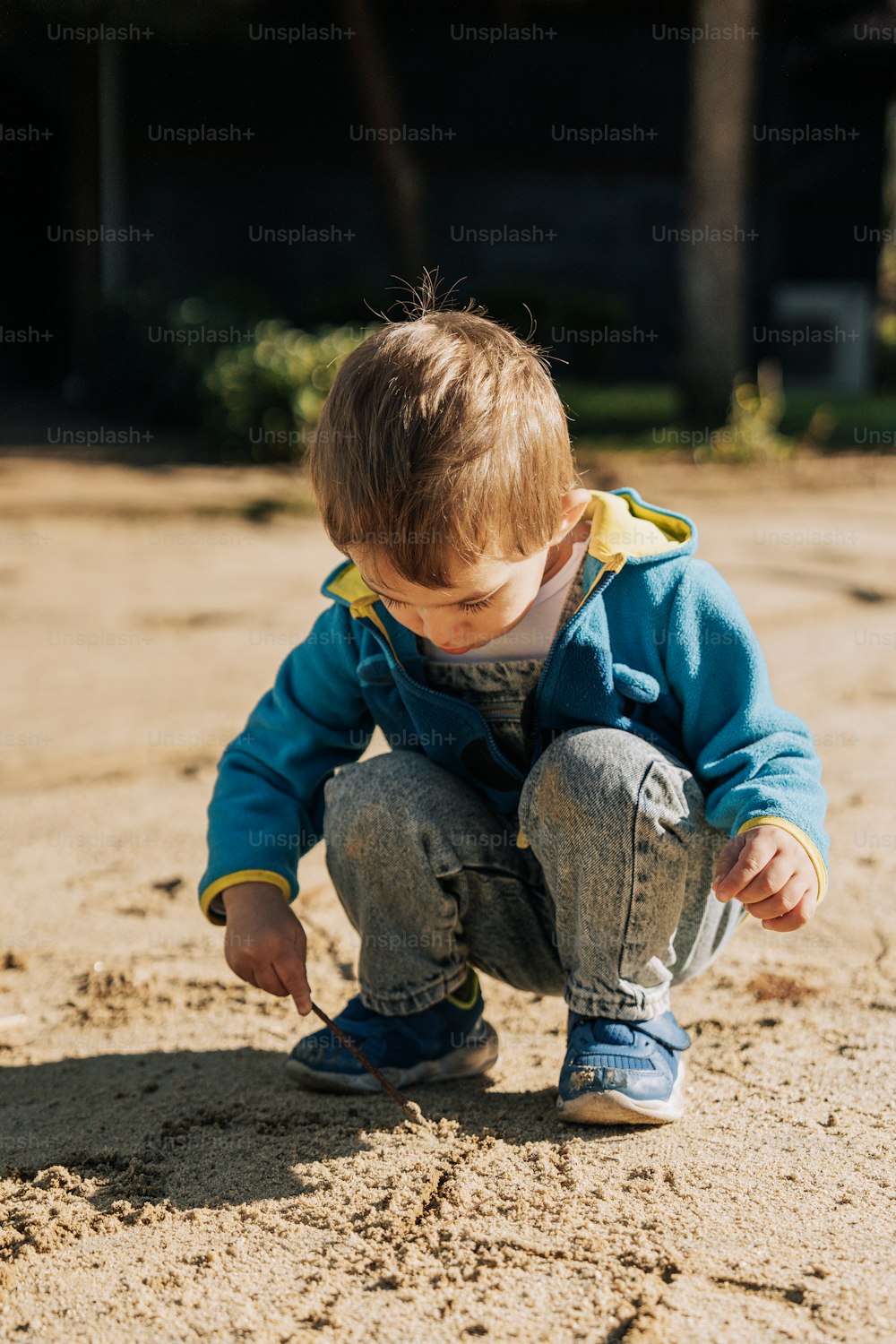 a small child in a blue jacket playing in the sand