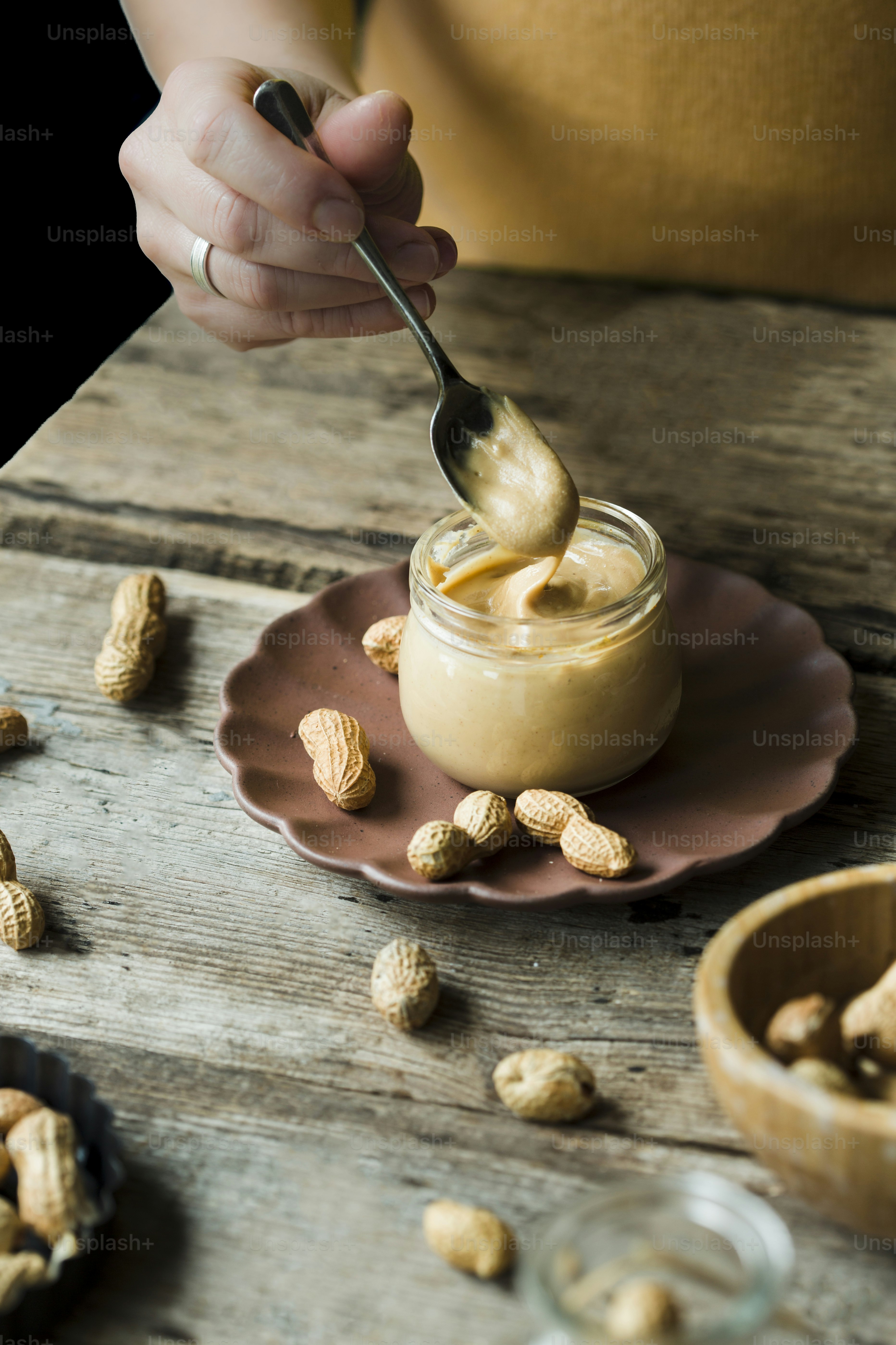 Eine Person taucht Erdnüsse in ein Glas Erdnussbutter