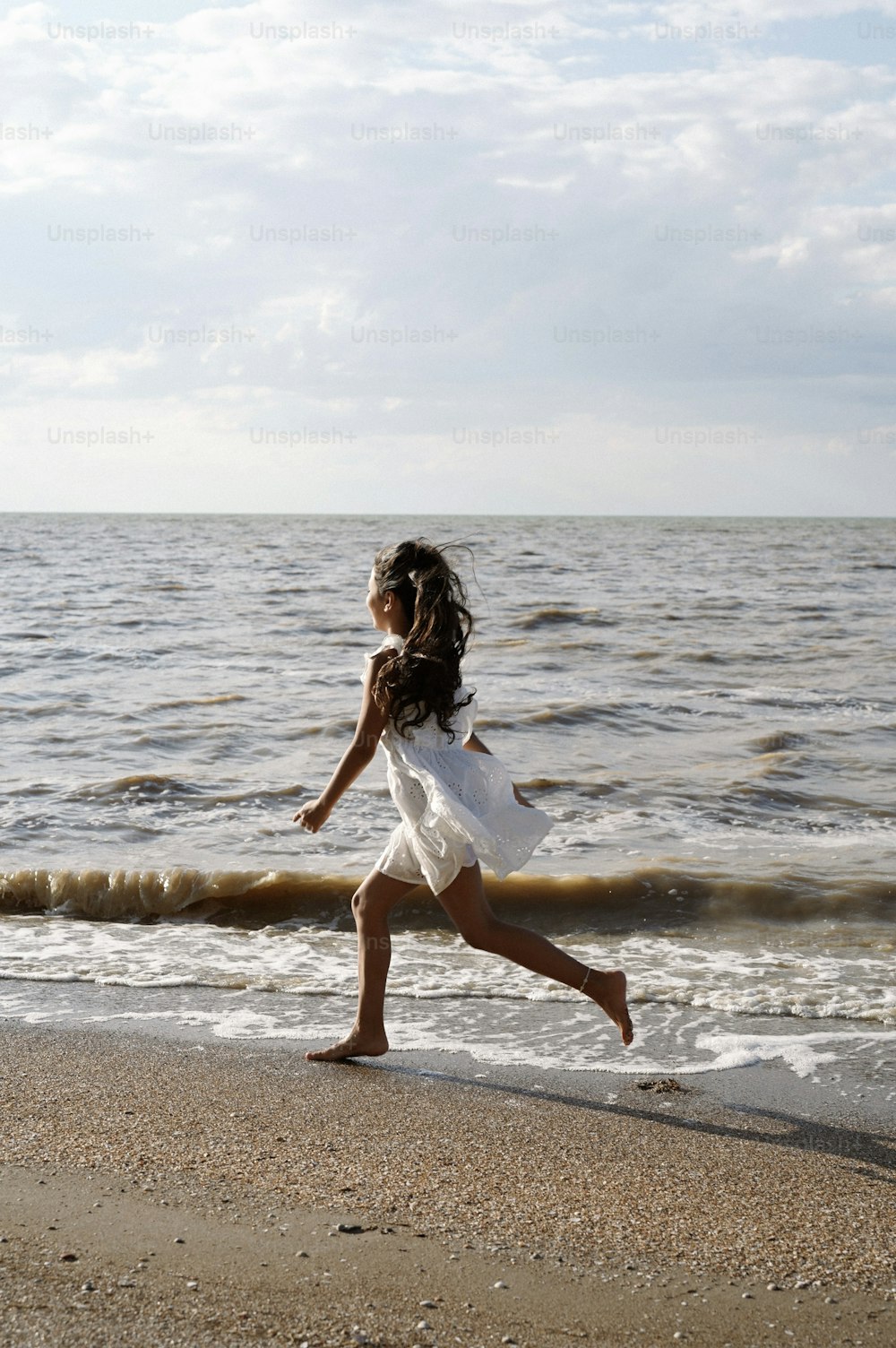 a young girl running along the beach towards the ocean