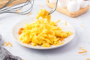 un piatto bianco condito con uova strapazzate accanto a una frusta di uova