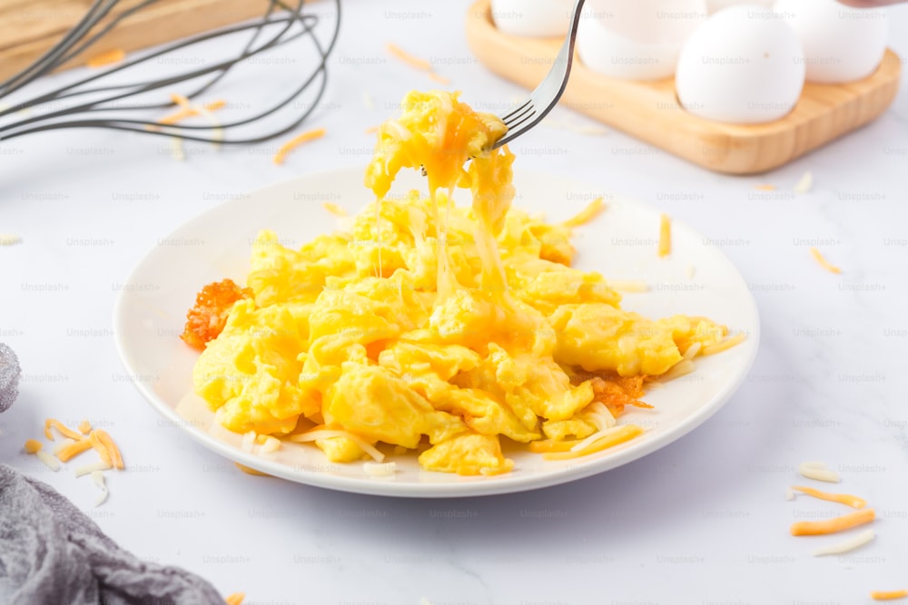 a white plate topped with scrambled eggs next to a whisk of eggs