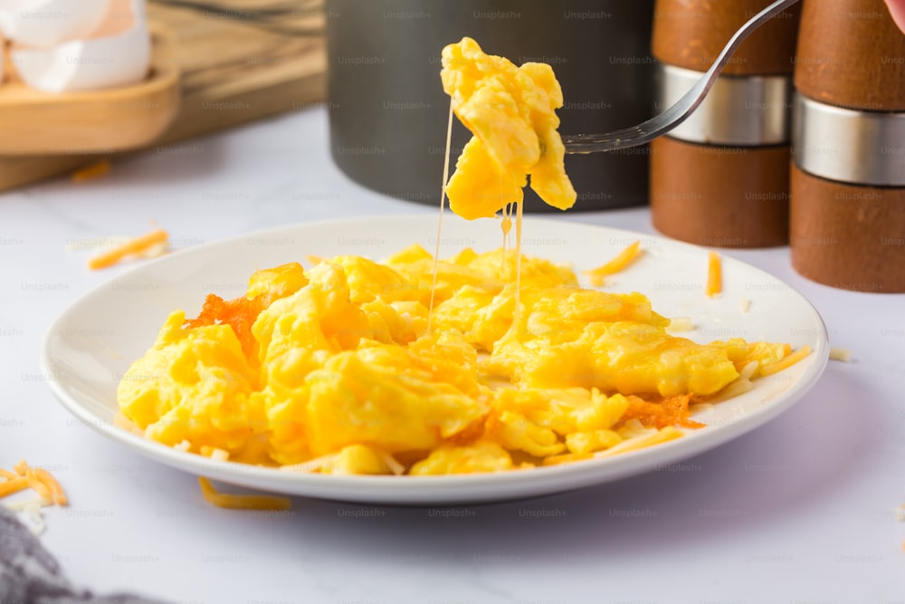 a plate of scrambled eggs being drizzled with a fork