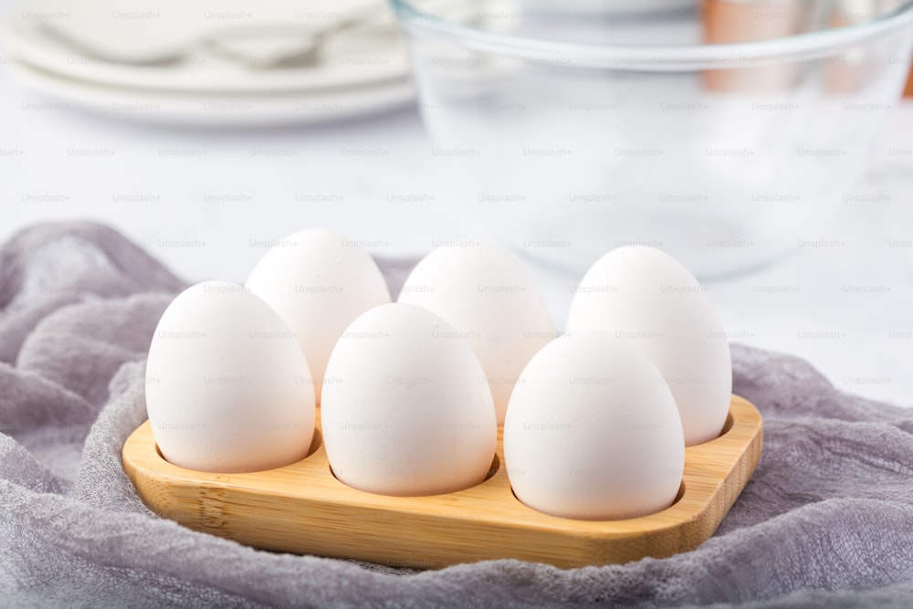 six white eggs in a wooden tray on a table