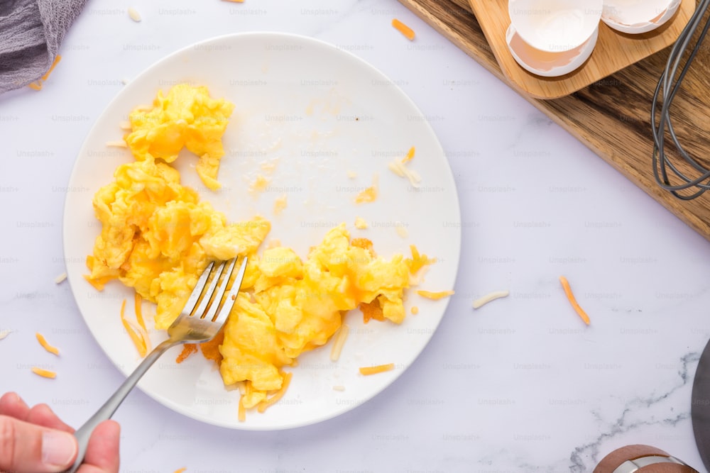 um prato branco coberto com ovos mexidos e um garfo