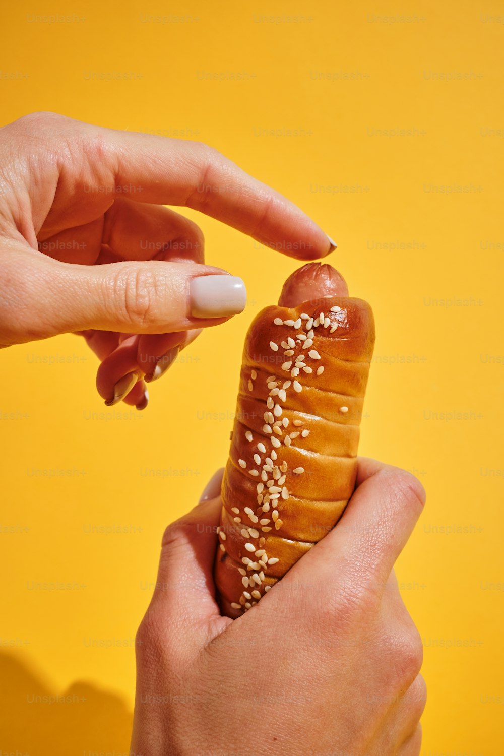 une personne tenant un pain à hot-dog avec des graines de sésame