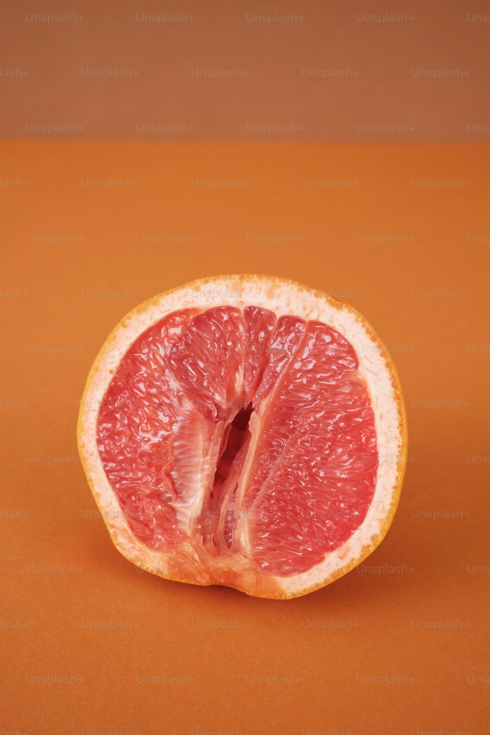 a grapefruit cut in half on an orange background