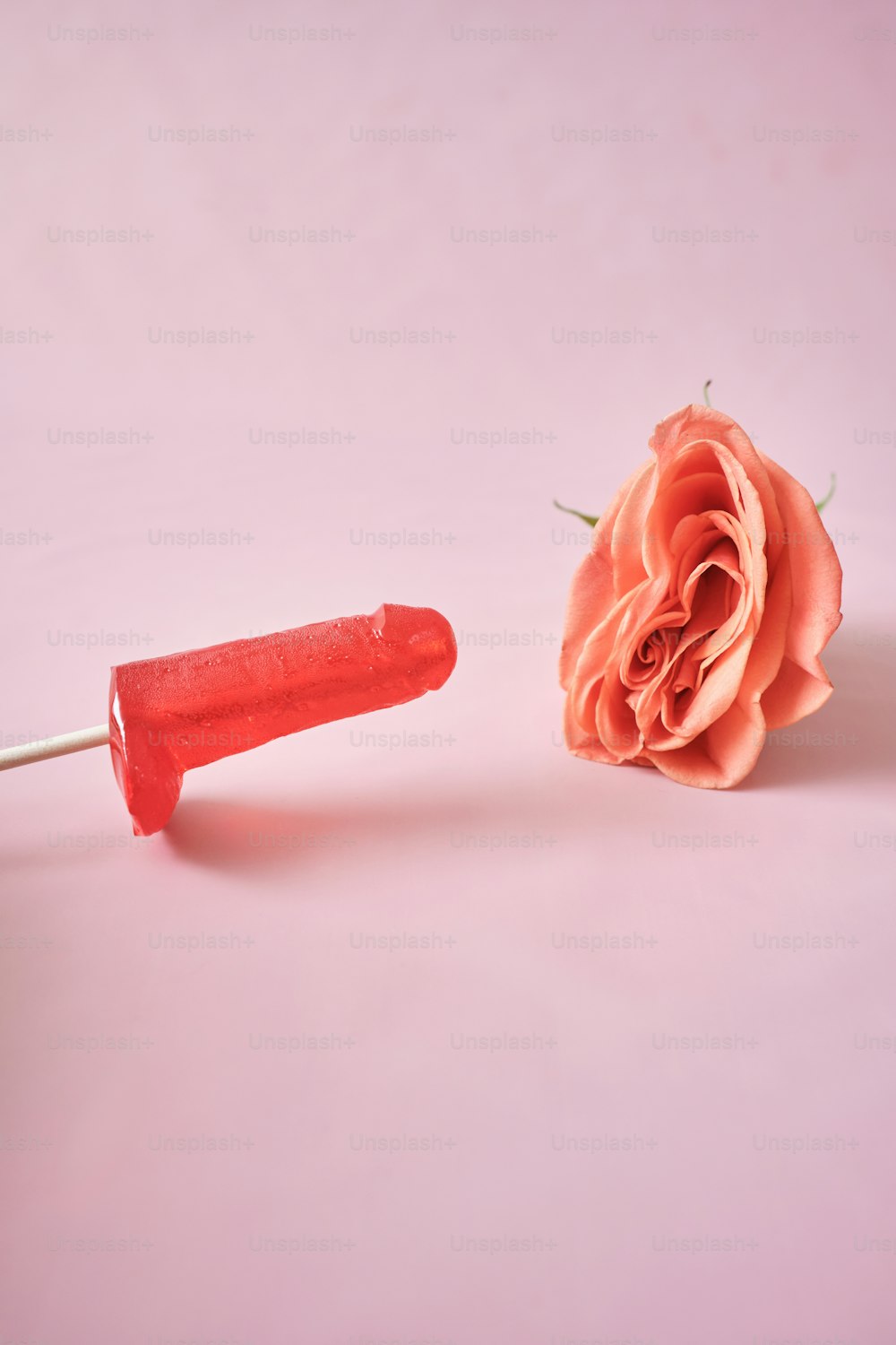 una rosa rosa y un objeto de plástico rojo sobre un fondo rosa