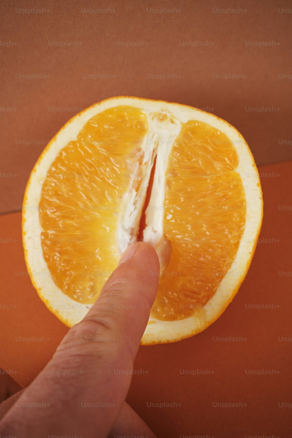 a hand pointing at an orange cut in half