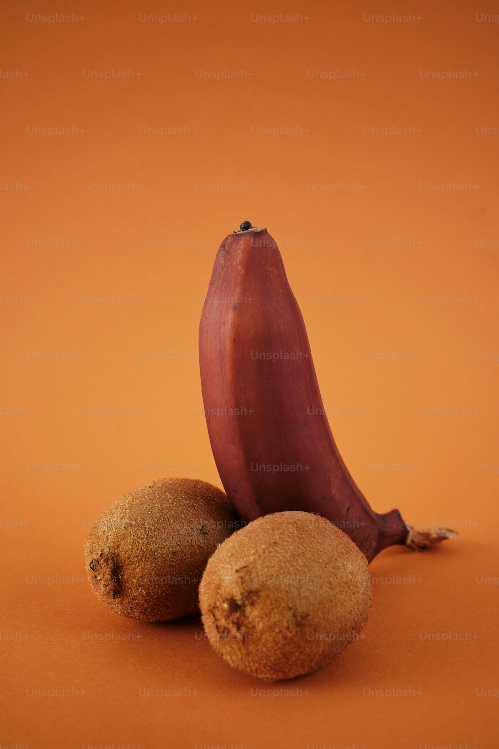eine Banane und zwei Kiwis auf orangefarbenem Hintergrund