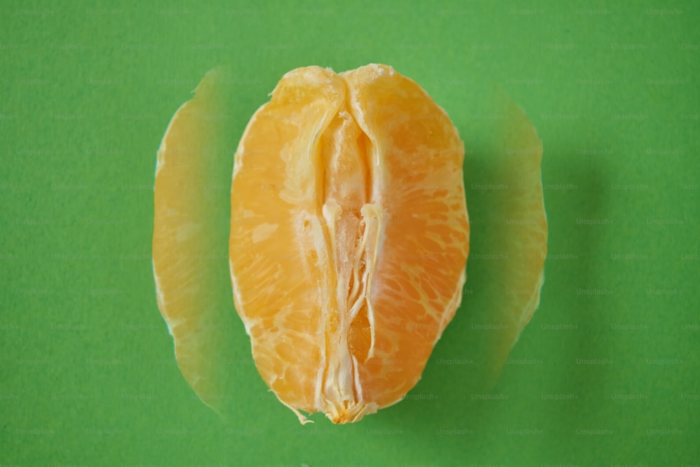 eine geschälte Orange, die auf einer grünen Oberfläche sitzt