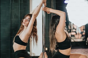 Zwei Frauen in schwarzen Sport-BHs tanzen Pole Dance