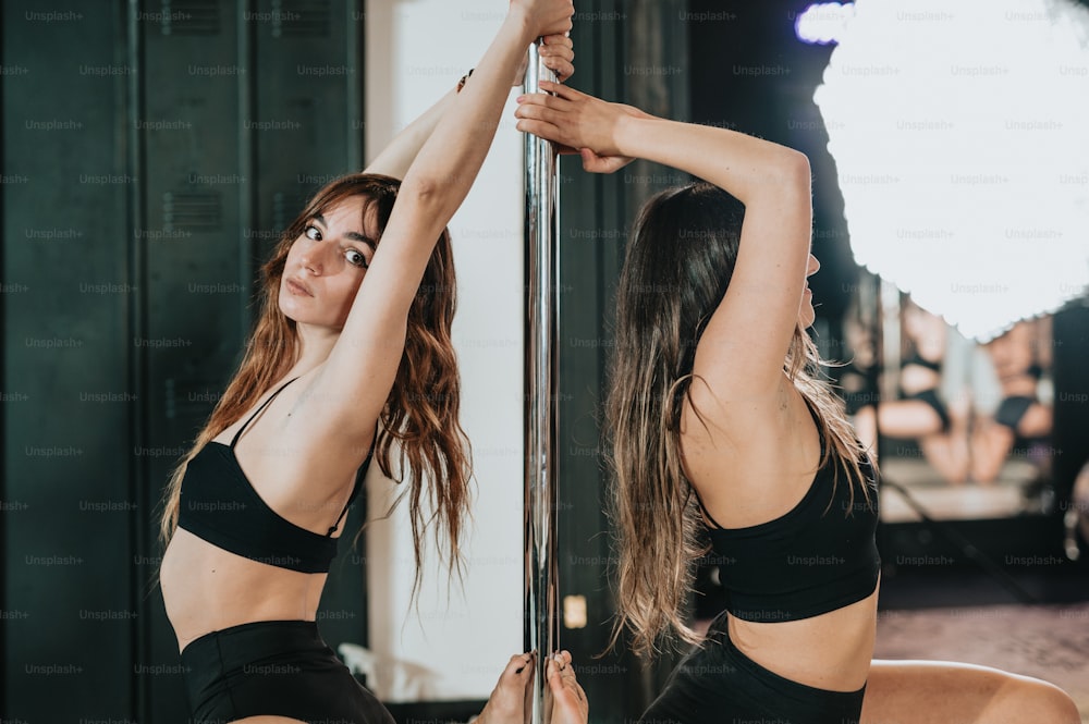 two women in black sports bras are doing pole dancing
