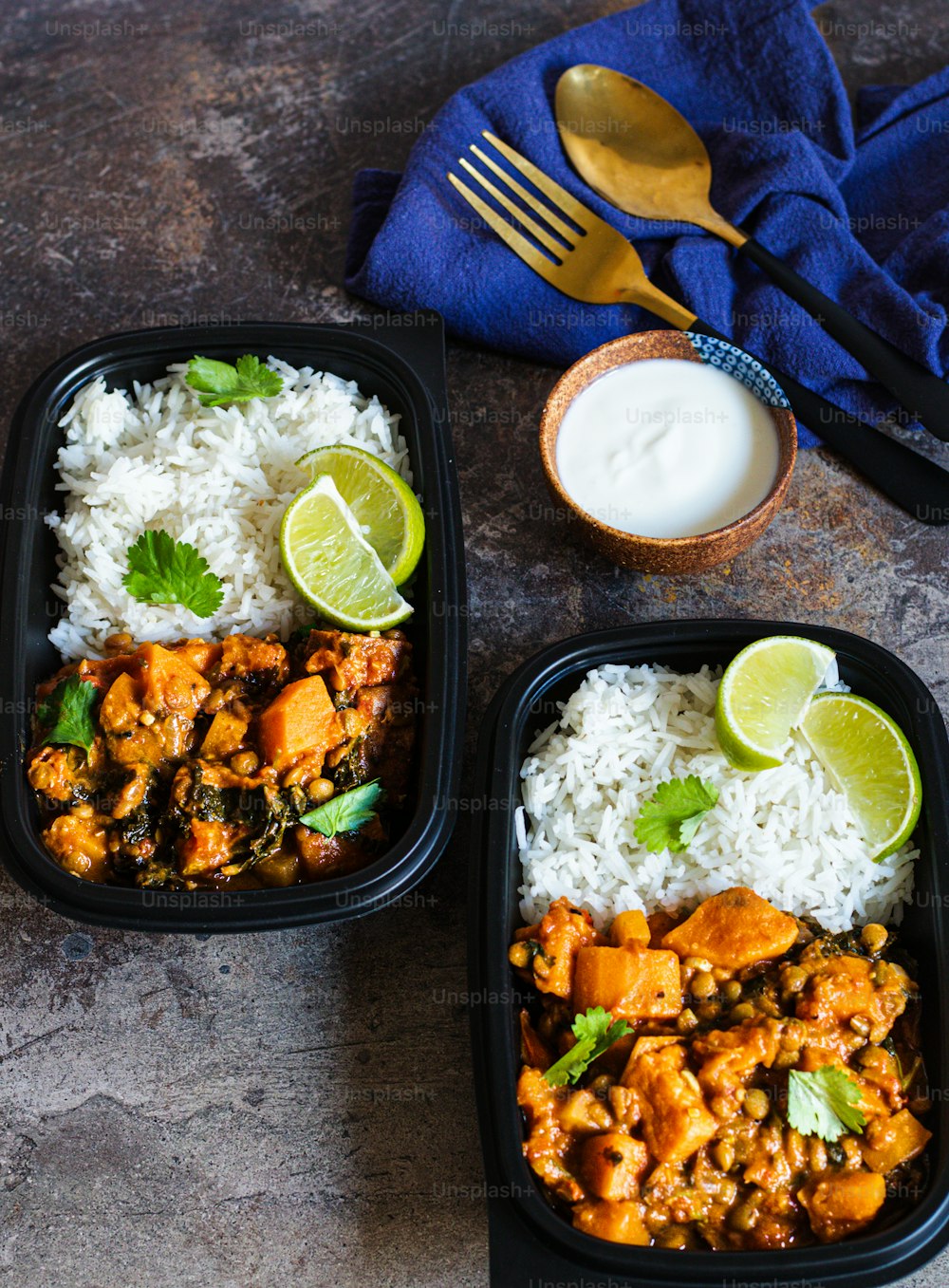 deux récipients noirs remplis de riz et de poulet au curry