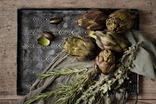 artichokes and herbs on a tray on a wooden table