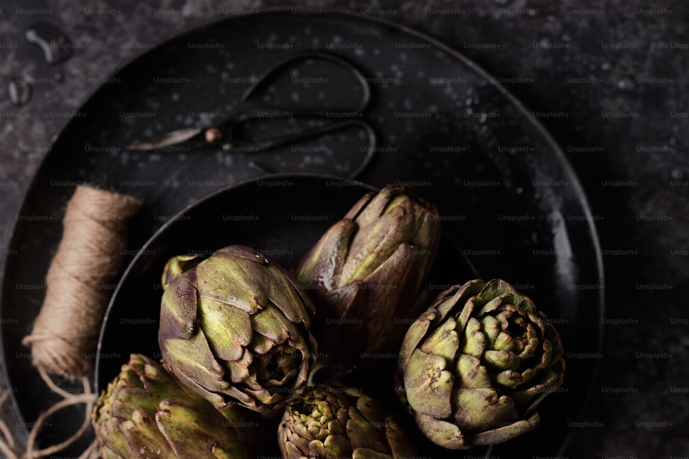 a black plate topped with artichokes next to a pair of scissors