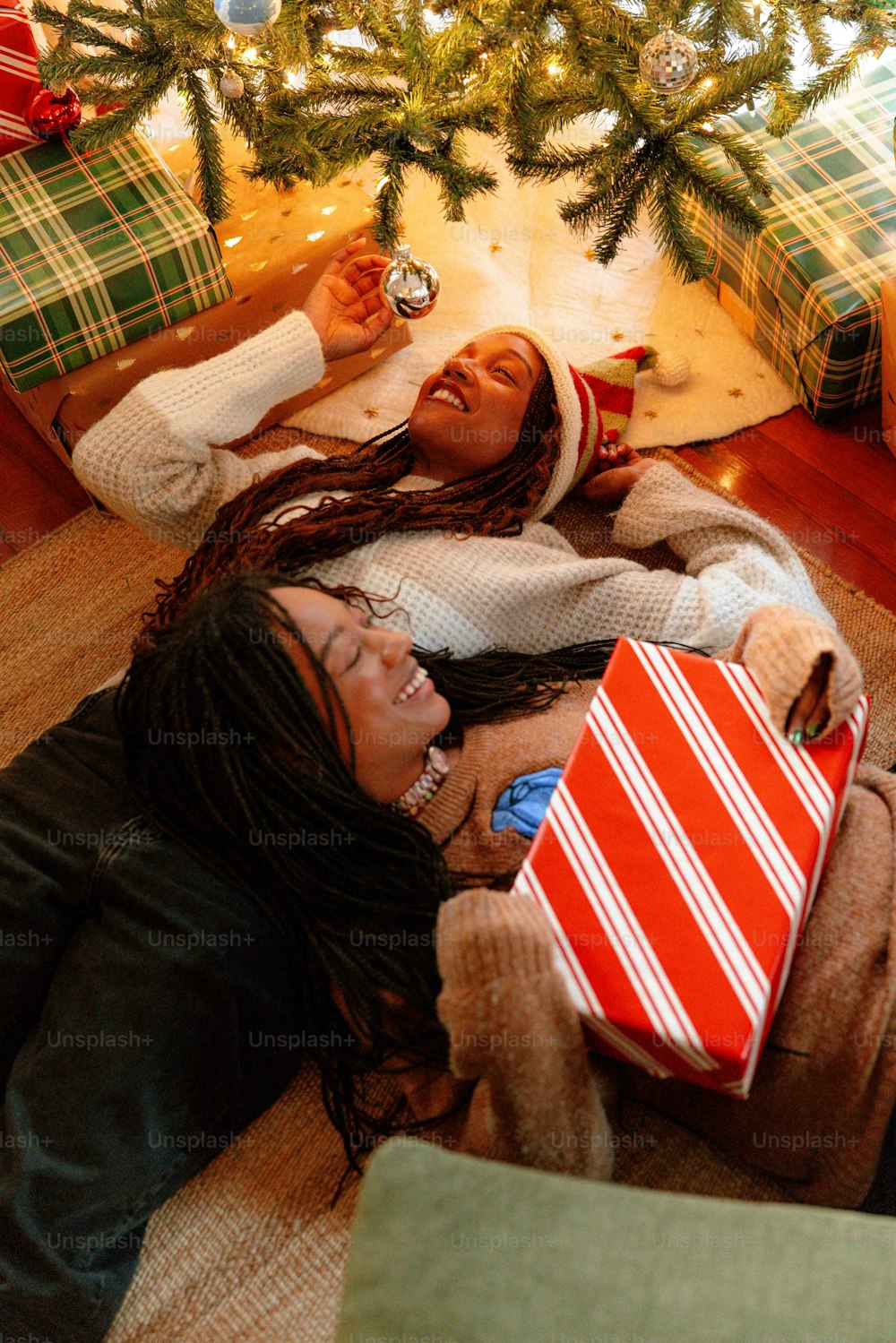 two women laying on the floor with presents under a christmas tree