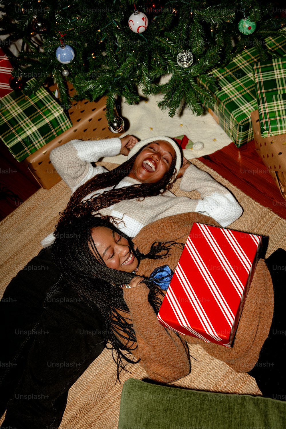 a couple of women laying next to a christmas tree