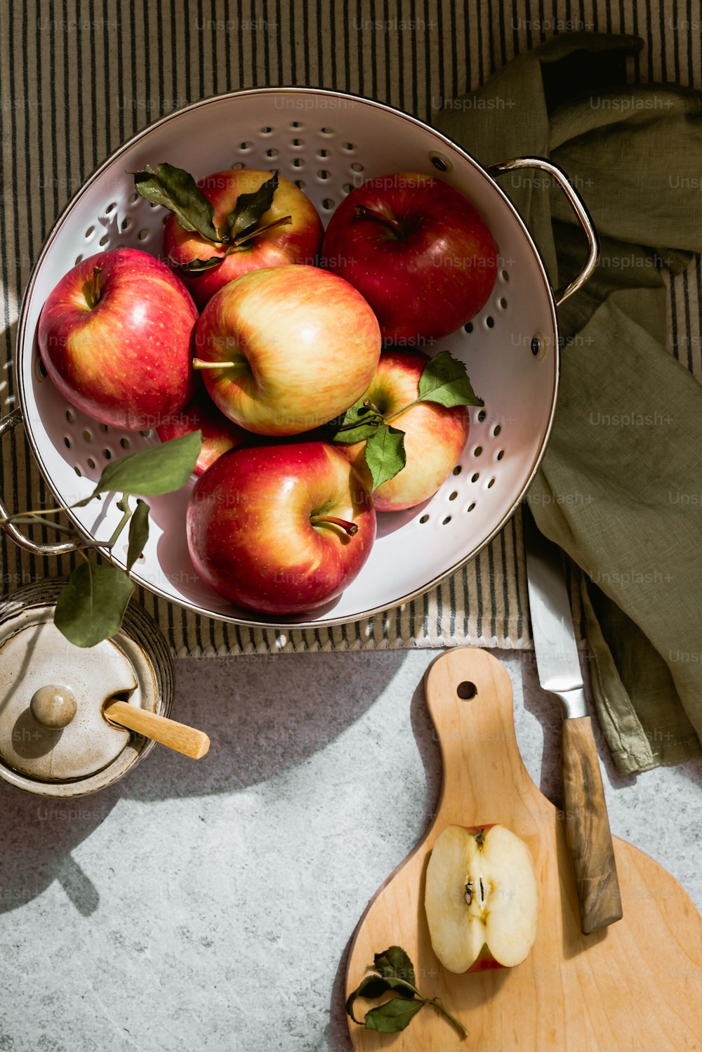 a bowl of apples sitting on a table next to a cutting board