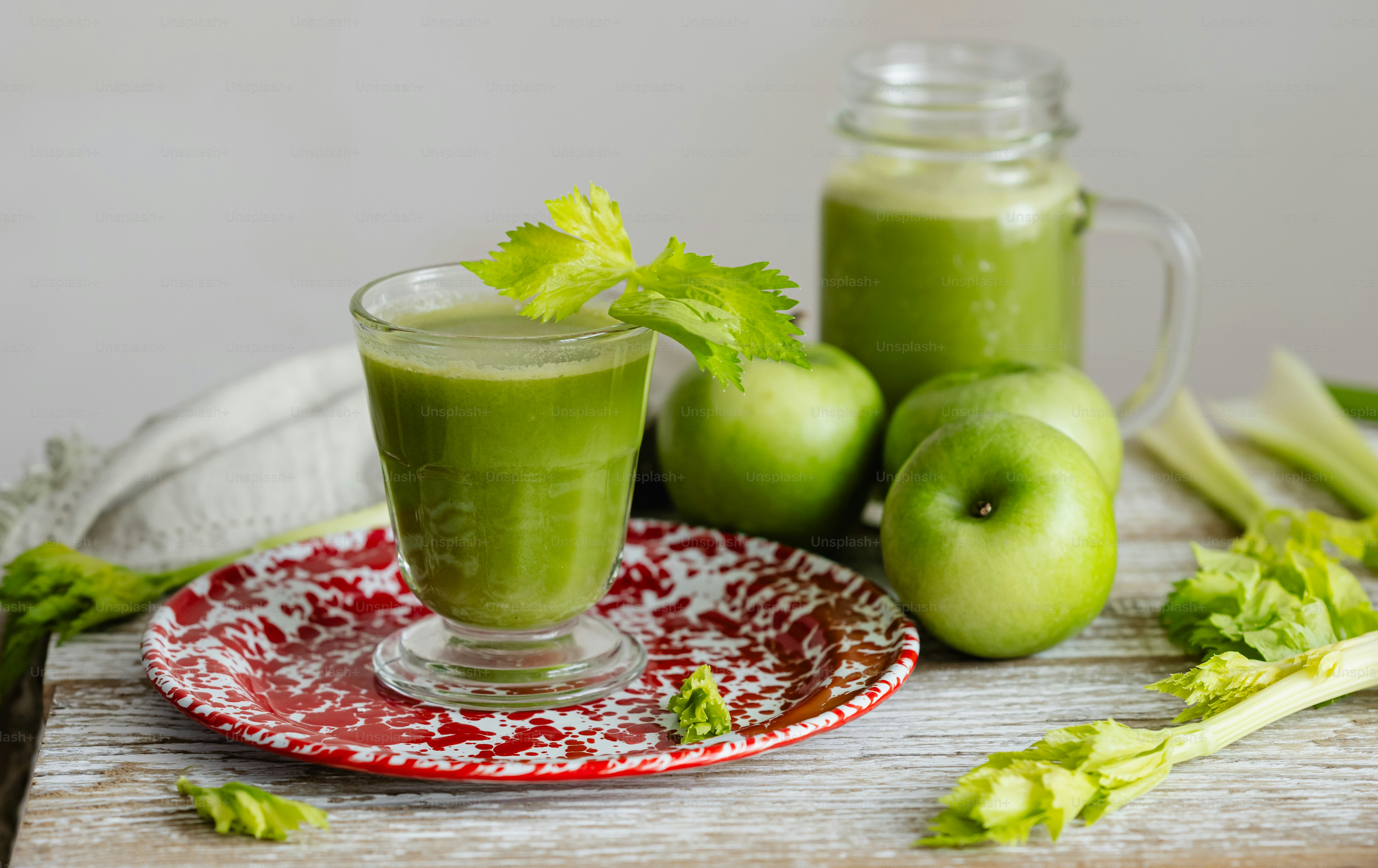 a glass of green smoothie with celery on a plate