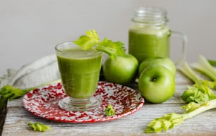 a glass of green smoothie with celery on a plate
