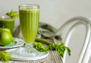 a glass of green juice sitting on top of a table