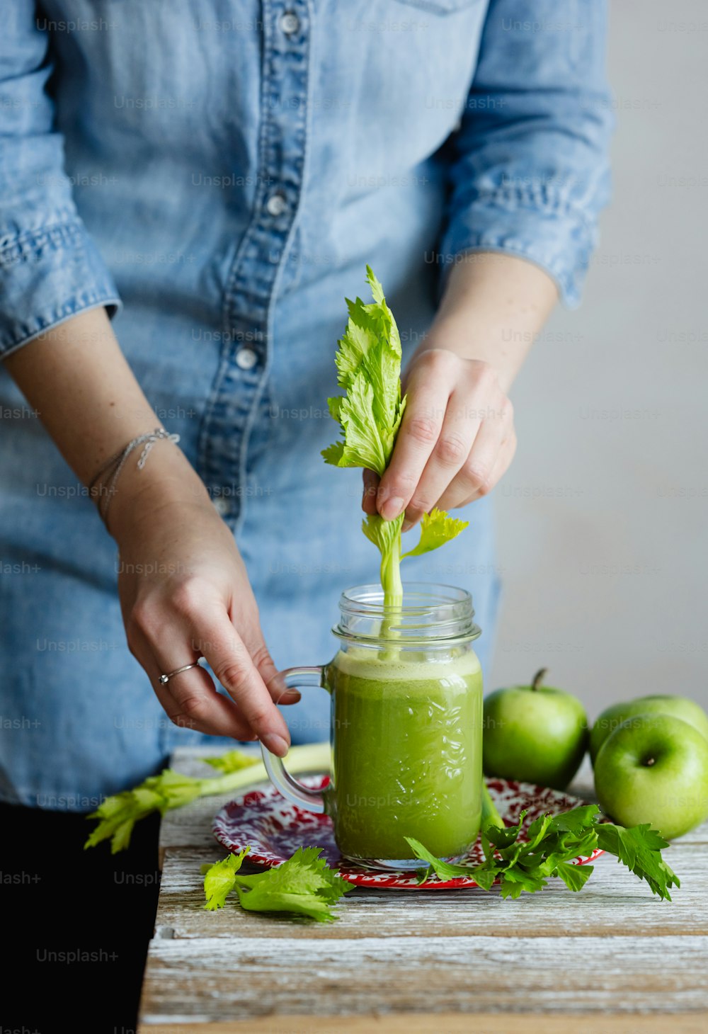 a woman putting a leaf in a jar of green smoothie