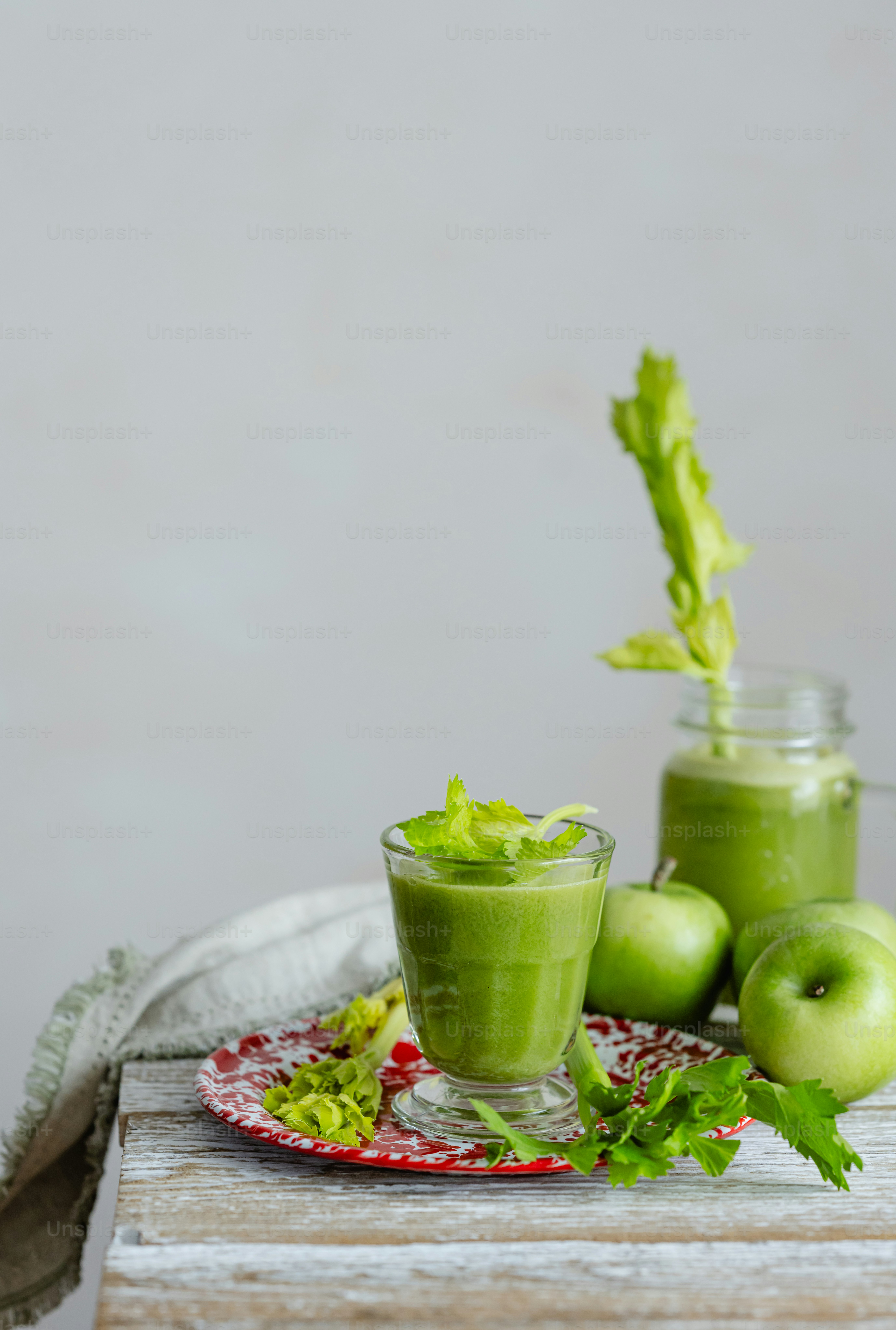 two glasses of green smoothie on a red and white plate