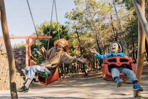 a boy and a girl sitting on swings in a park