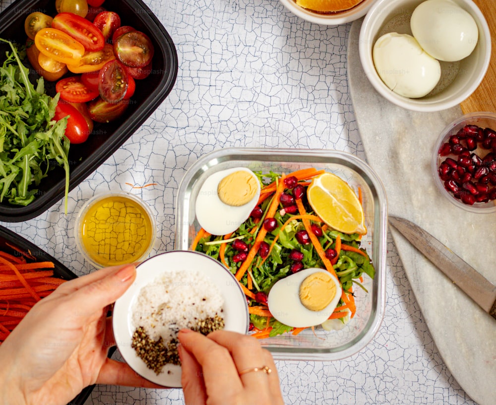 a person holding a plate of food next to bowls of vegetables and eggs