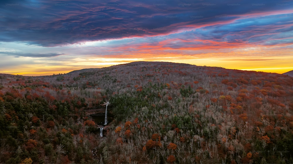 a sunset view of a mountain with a waterfall in the foreground